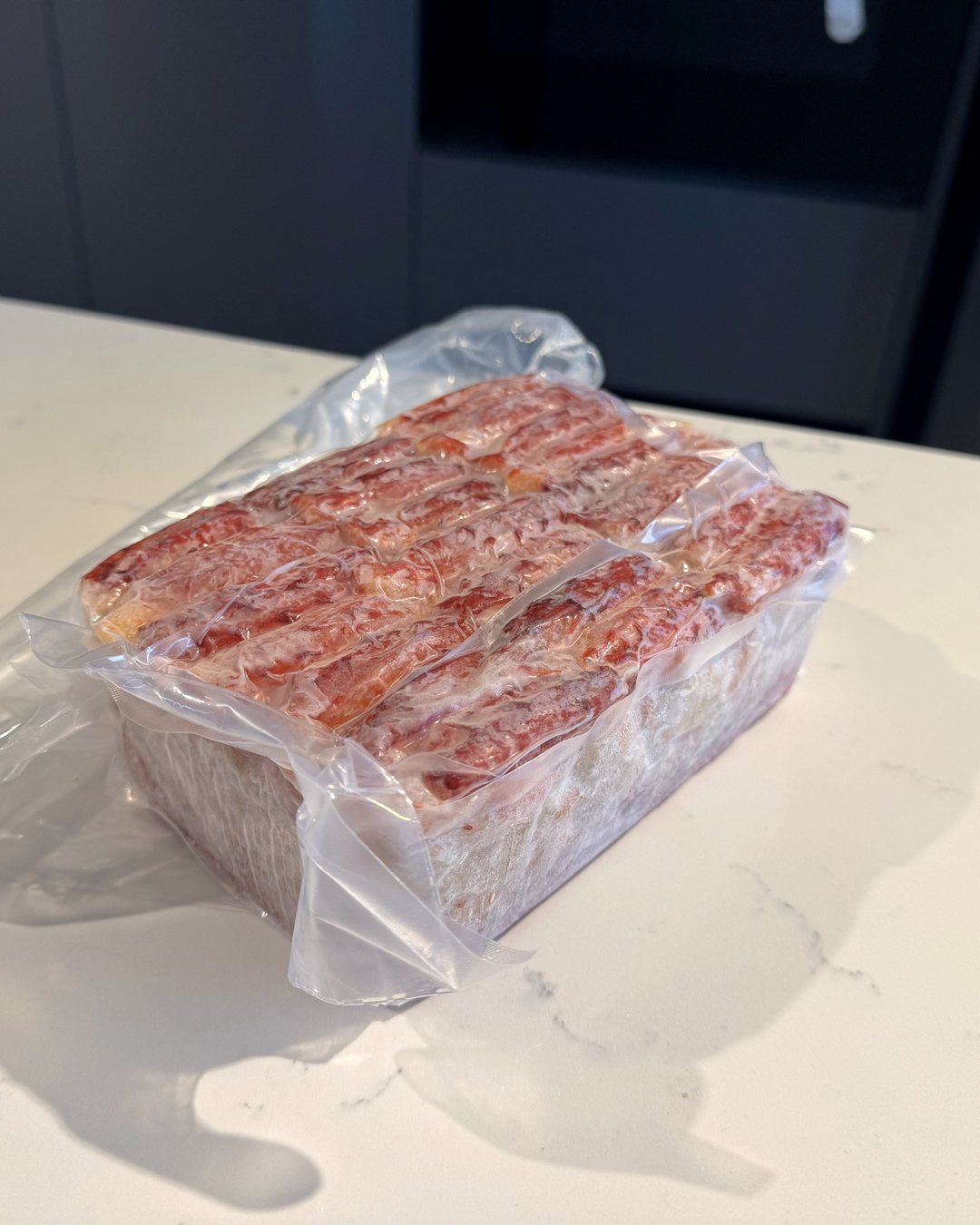 Foto real: bloque congelado de carne de centolla en su bolsa al vacío, con las patas rojas en filas